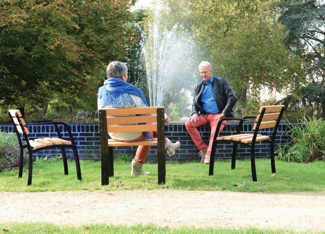 2 Menschen sitzen auf Seniorensitzen in einem Park vor einem Springbrunnen