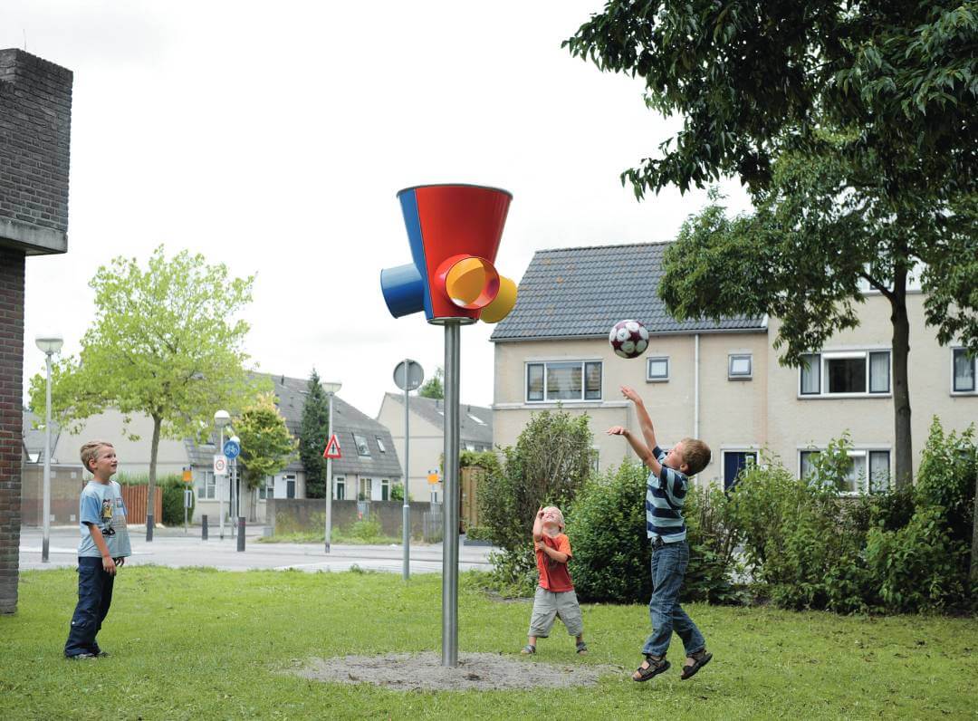 Drei Kinder spielen in einem Wohngebiet und werfen einen Ball in einen bunten Balltrichter