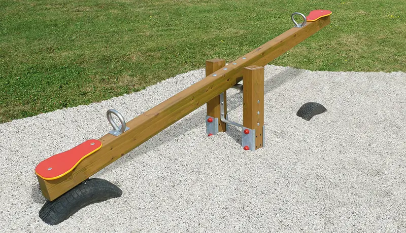 Holz-Wippe mit roten Sitzen und Metallgriffen, montiert auf zwei Reifen, auf Kiesfläche im Freien.