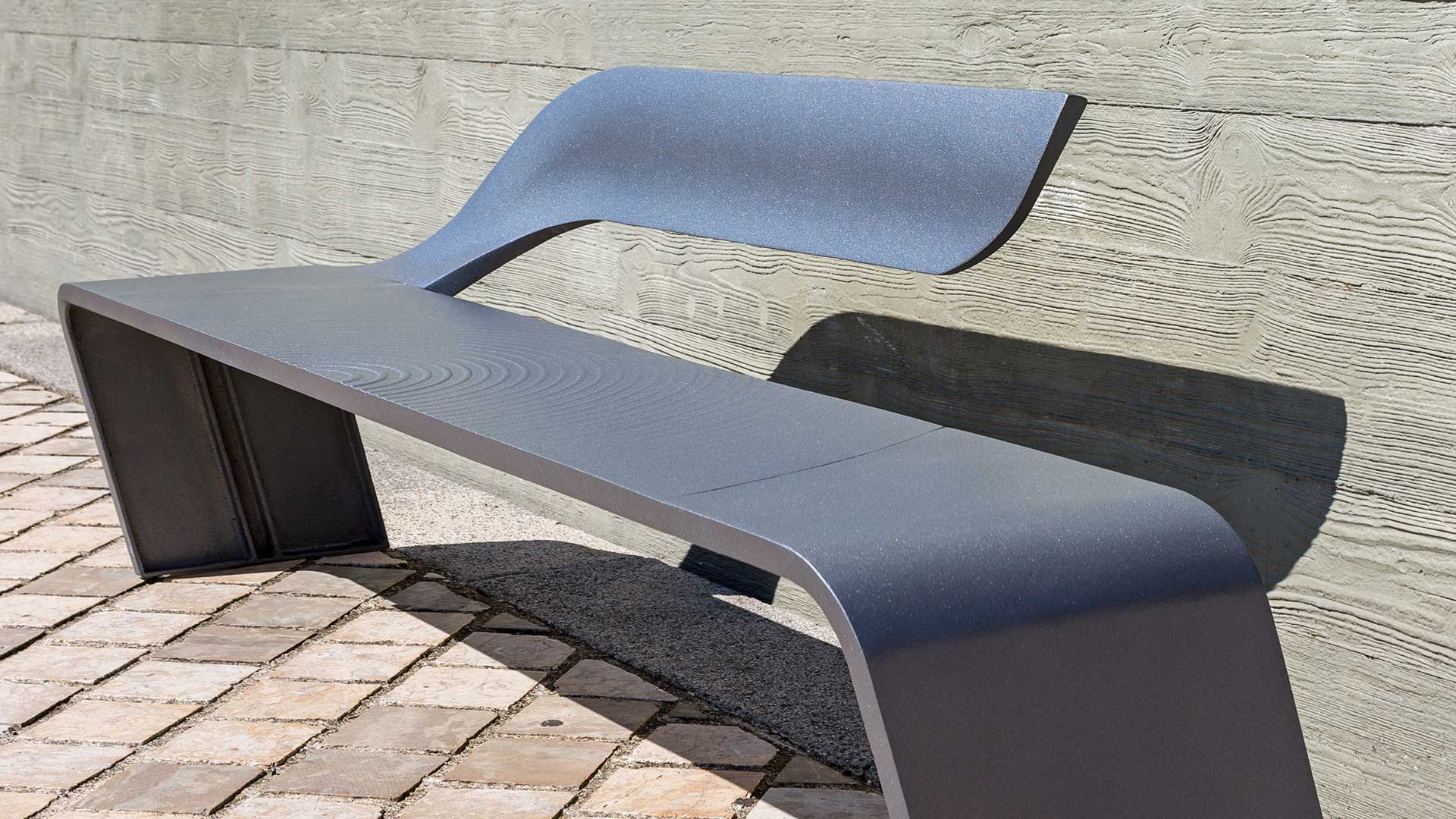 Moderne Sitzbank aus Aluminiumguss mit geschwungenem Design auf gepflastertem Untergrund