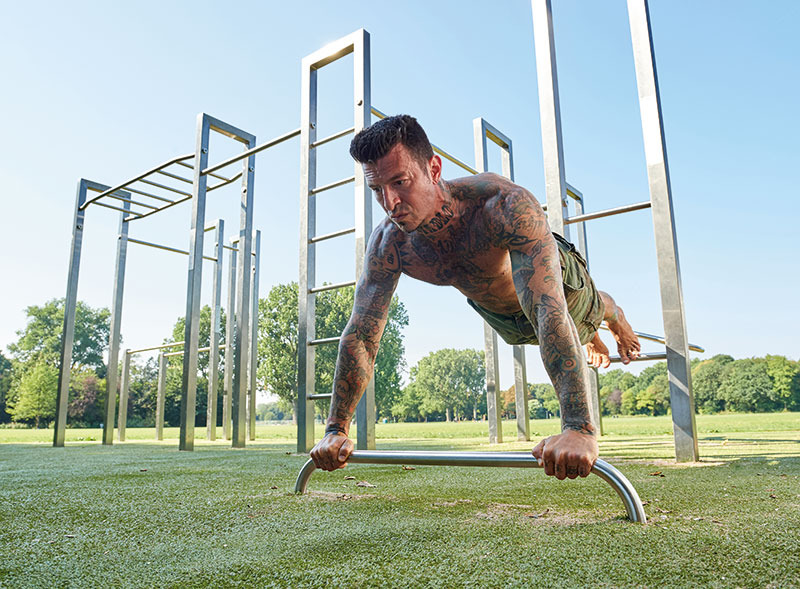 Sportlicher Mann macht Liegestütze an einer Calisthenics Anlage