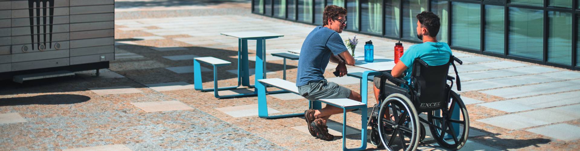 Zwei Personen sitzen an einem barrierefreien Picknicktisch vor einem modernen Glasgebäude