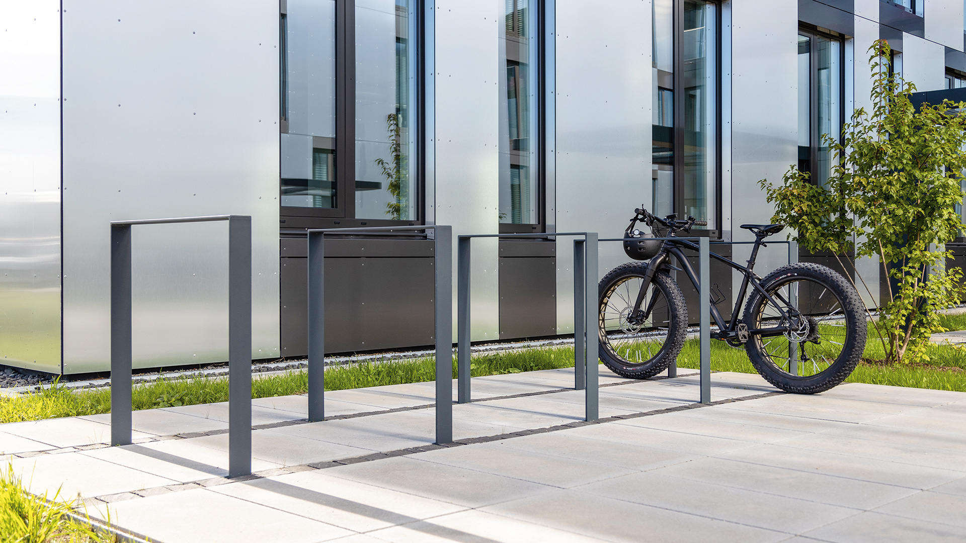 Mehrere Fahrradanlehnbügel vor einem Gebäude, an einem der Fahrradanlehnügel ist ein Fahrrad angelehnt
