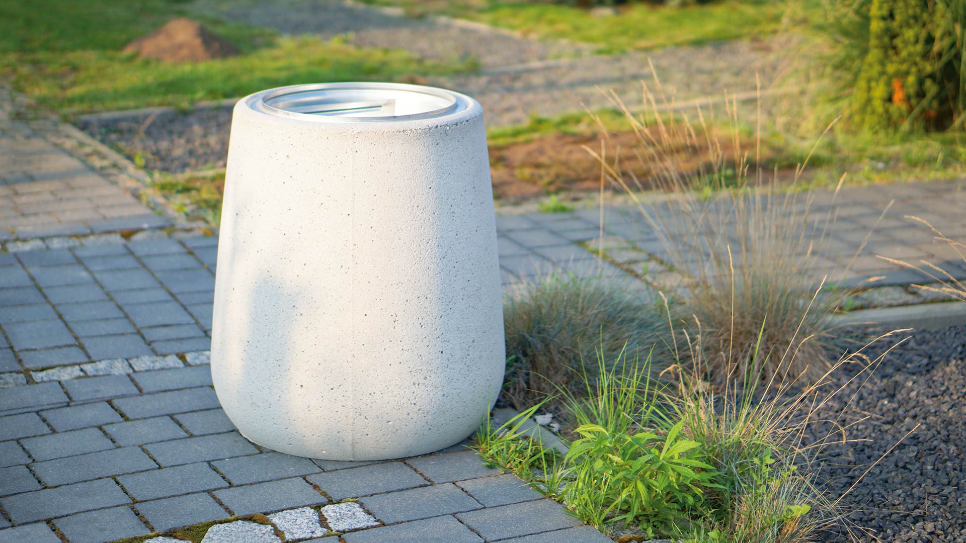 Moderner, weißer Müllbehälter aus Beton auf einem gepflasterten Weg