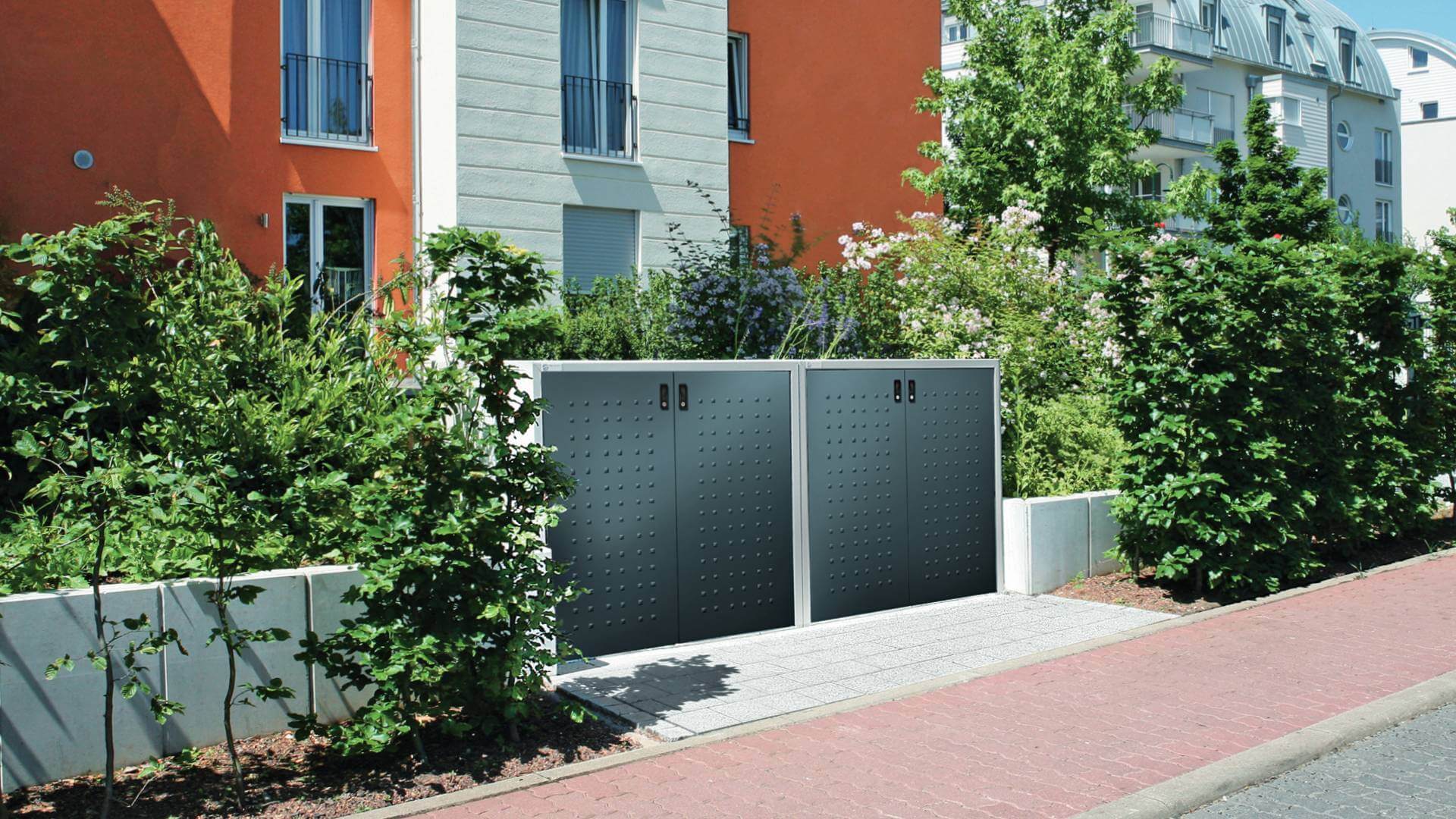Zwei Mülltonnenboxen aus Metall vor einem Wohngebäude