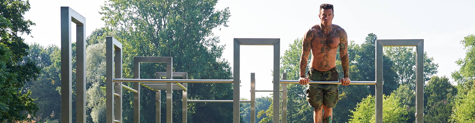 Mann trainiert an einer Calisthenics-Anlage im Freien mit mehreren Reckstangen und Rahmen