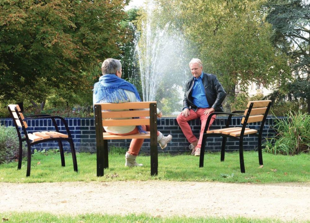 2 Menschen sitzen auf Seniorensitzen in einem Park vor einem Springbrunnen