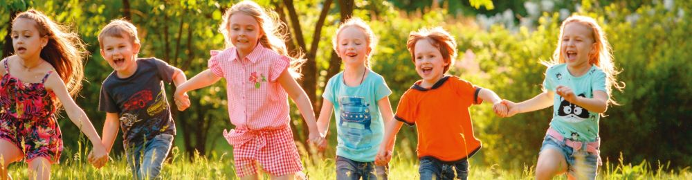 Kinder laufen Hand in Hand über eine Wiese 