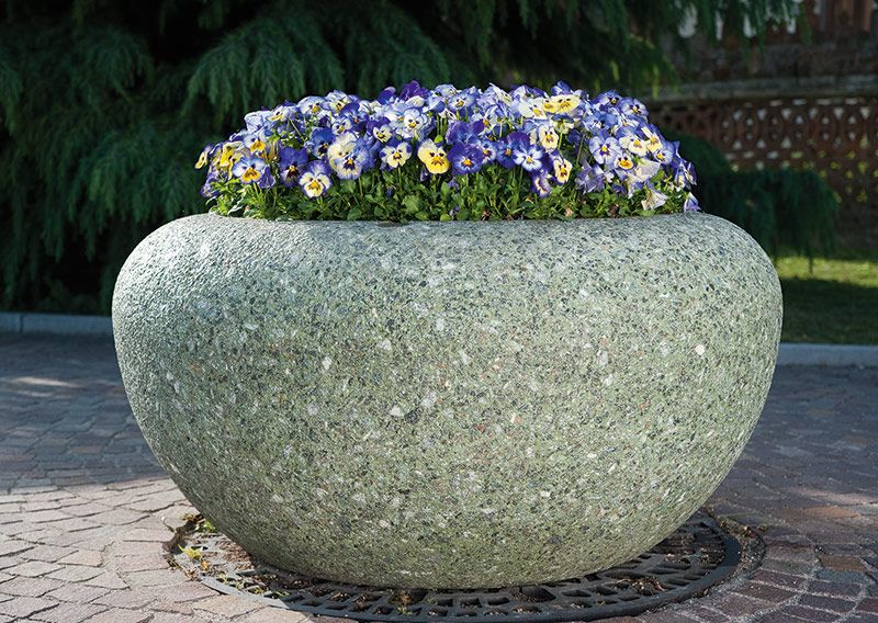 Großer runder Marmor-Pflanzbehälter mit blühenden Stiefmütterchen auf gepflastertem Boden