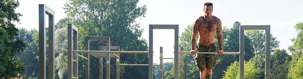 Mann trainiert an einer Calisthenics-Anlage im Freien mit mehreren Reckstangen und Rahmen