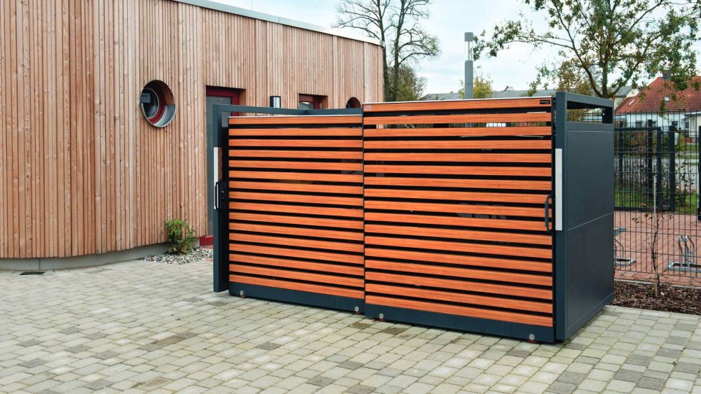 Mülltonnenbox it Holzoptik auf einem gepflasterten Platz
